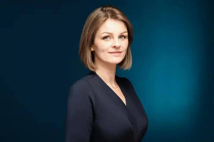 Profesjonalne zdjęcie do CV: uśmiechnięta kobieta z krótkimi blond włosami, w granatowej bluzce, na ciemnoniebieskim tle.