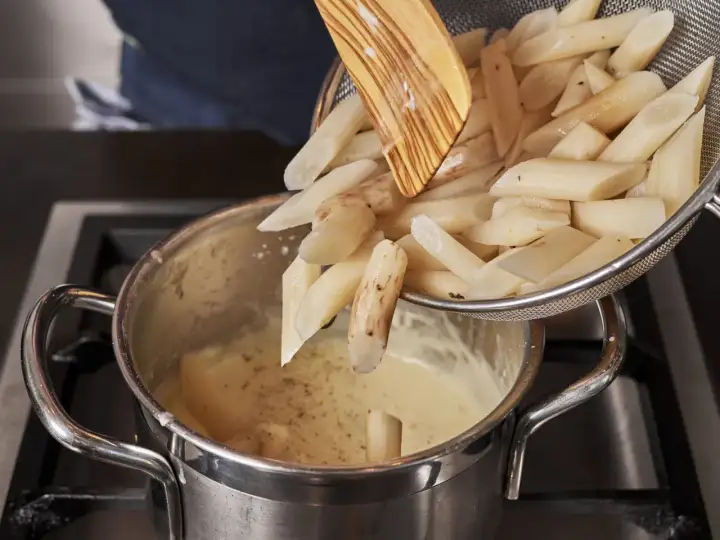 Schwarzwurzeln werden für ein leckeres Rezept in eine cremige Sauce gegeben. Ein Holzlöffel hilft beim Einfüllen.