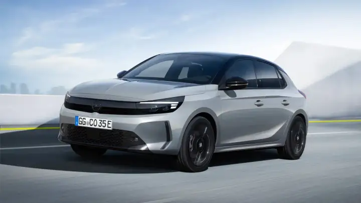Grå Opel Corsa-e testkörs på en väg med en modern bakgrund.
