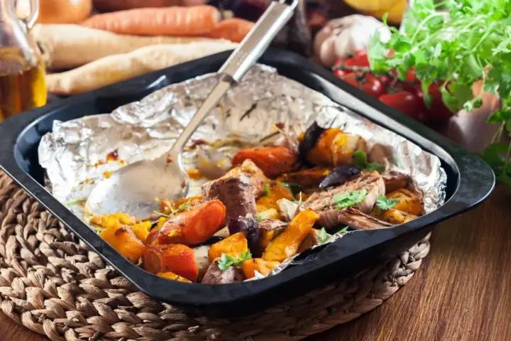 Szybkie danie z piekarnika: pieczone warzywa korzeniowe, dynia i mięso w folii aluminiowej, gotowe do podania.