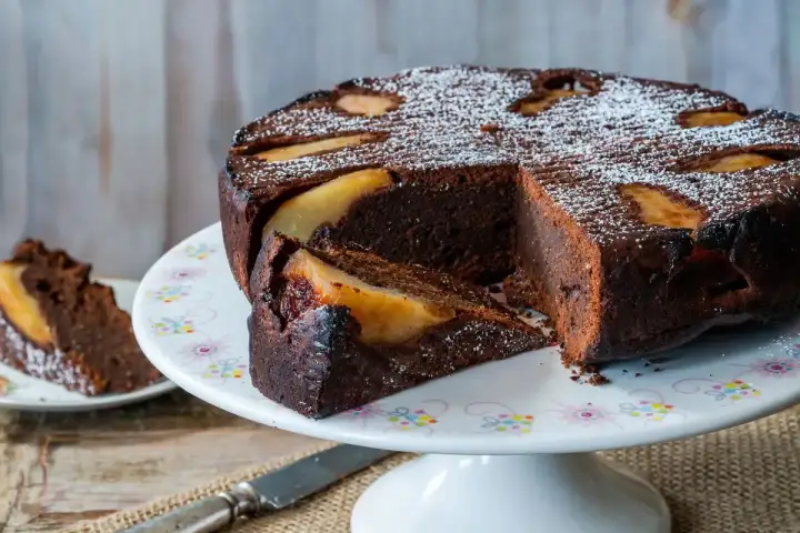 Deliziosa torta pere e cioccolato, con una fetta tagliata e cosparsa di zucchero a velo.