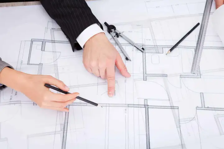 Rysunki techniczne domu, na których dwie osoby omawiają zmianę projektu po uzyskaniu pozwolenia na budowę.