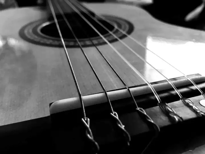 Zbliżenie na gitarę, gdzie widoczne są napięte struny. Ich metaliczny połysk i sposób mocowania przy mostku sugerują gotowość do wydobycia pięknych dźwięków.