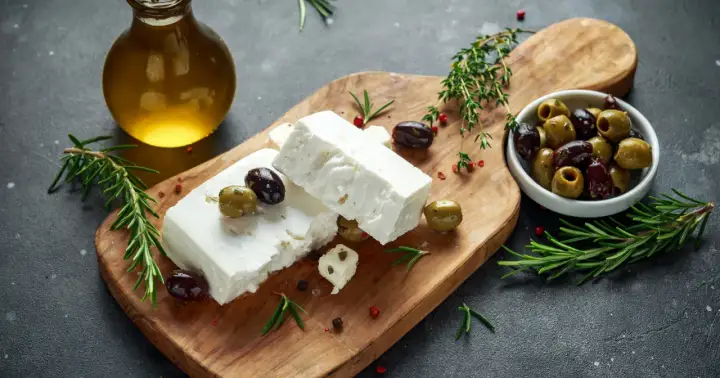 Kostki sera feta, oliwki, rozmaryn i oliwa z oliwek na desce. Idealne do sałatki, a feta kcal nie są tak wysokie.
