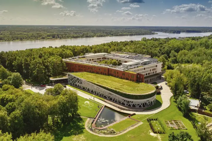 Nowoczesny hotel nad Narwią z zielonym dachem i stawem, otoczony lasem. Idealne miejsce na wypoczynek.