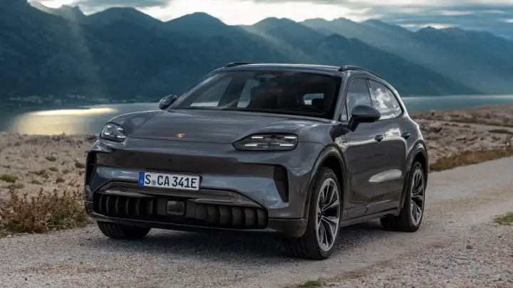 Szary Porsche Cayenne 2025 na kamienistej drodze z widokiem na góry i jezioro.