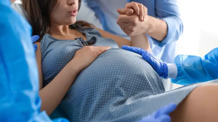 Mujer dando a luz en un parto natural, apoyada por su pareja y personal médico.