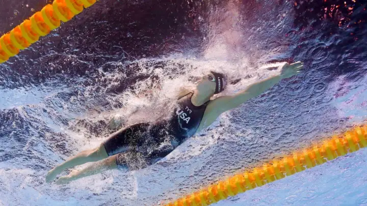 Katie Ledecky training underwater, powering through the water in a USA swimsuit.