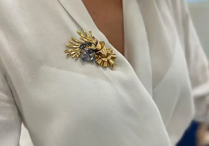 Una joya en forma de broche de oro con zafiros y diamantes, adornando una blusa blanca.