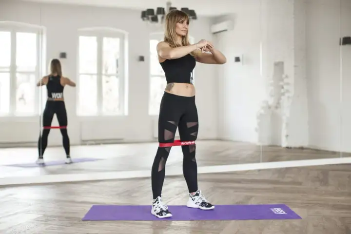 Kobieta wykonuje ćwiczenia z gumami mini band, wzmacniając mięśnie nóg.