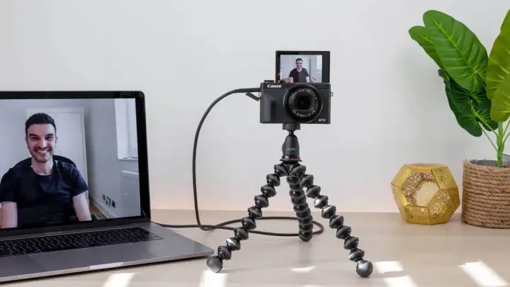 Ustawienie do streamingu: aparat Canon G7X na statywie Joby, podłączony do laptopa. Widoczny uśmiechnięty mężczyzna na ekranie. Idealne do streamingu z użyciem **EOS Utility**.