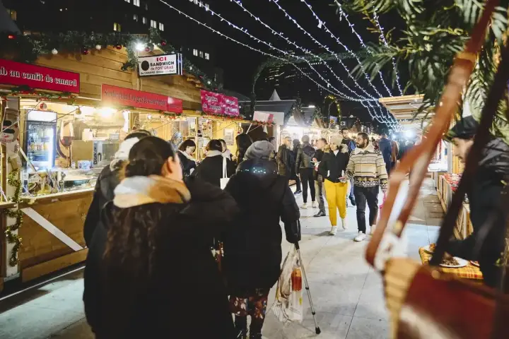 Ambiance féerique d'un marché de Noël à Paris. Des chalets en bois illuminés proposent des spécialités, tandis que des passants flânent sous les guirlandes lumineuses.