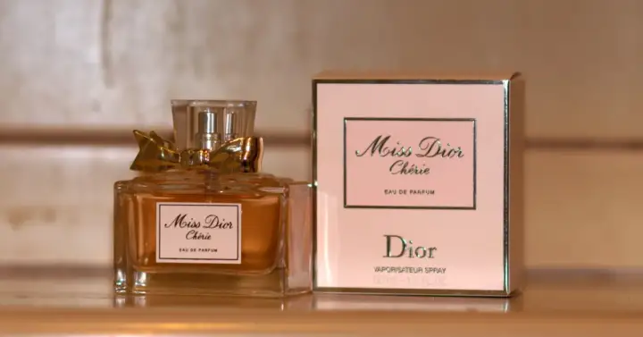 Elegancka butelka i pudełko perfum Miss Dior Chérie, ozdobione złotą kokardką, emanują luksusem.