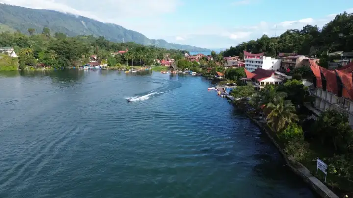 Ein Boot rast über den See, während man die Hügel und Häuser von Sumatra beim Backpacking genießt.