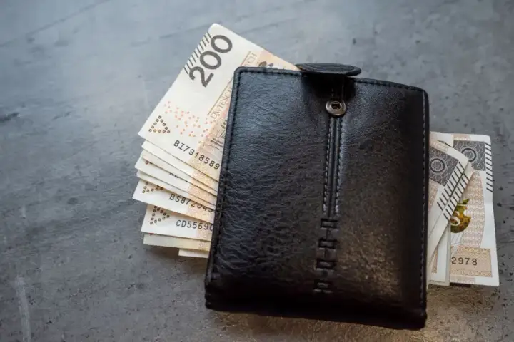 Czarny portfel z polskimi banknotami. Zastanawiasz się, jak obliczyć chorobowe w ciąży? Finanse przyszłej mamy.