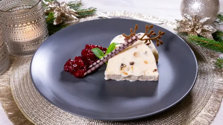 Ein festlicher weihnachts nachtisch: Eisparfait mit Beerenkompott, Schokoladenstäbchen und Rentiergeweih-Dekoration.