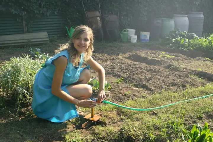 Dziewczyna w niebieskiej sukience podlewa grządki. Idealna ziemia pod uprawę jagody kamczackiej.