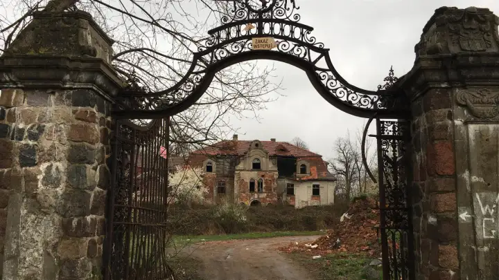 Zrujnowany pałac w glince, zniszczona brama i dziki ogród.