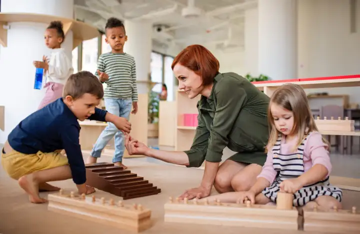 Niños y maestra en el suelo, aprendiendo con materiales didácticos. Las rutinas diarias en el aula fomentan el desarrollo.