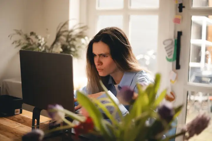 Zmarszczona kobieta przy laptopie, sfrustrowana z powodu braku połączenia z internetem.
