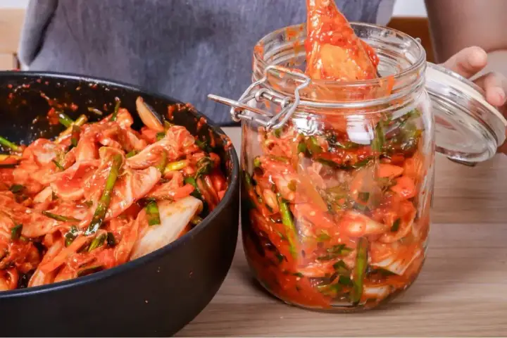 Przygotowanie kimchi: kapusta pekińska z sosem czosnkowo-paprykowym w misce i słoiku.