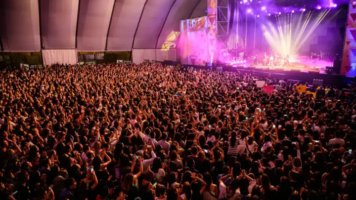 Multitud vibrante en concierto, con luces de escenario y carteles. Se aprecia la **autorización menores espacio Zity** en un cartel.
