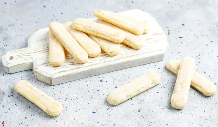 Savoiardi pronti per la ricetta del tiramisù, disposti su un tagliere bianco.