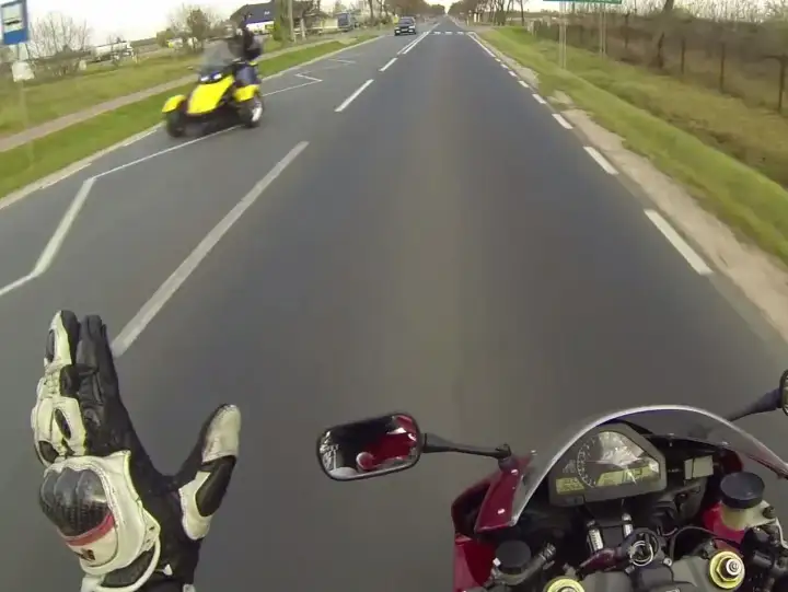 Pozdrowienie motocyklistów na drodze. Żółty pojazd trójkołowy mija motocyklistę.