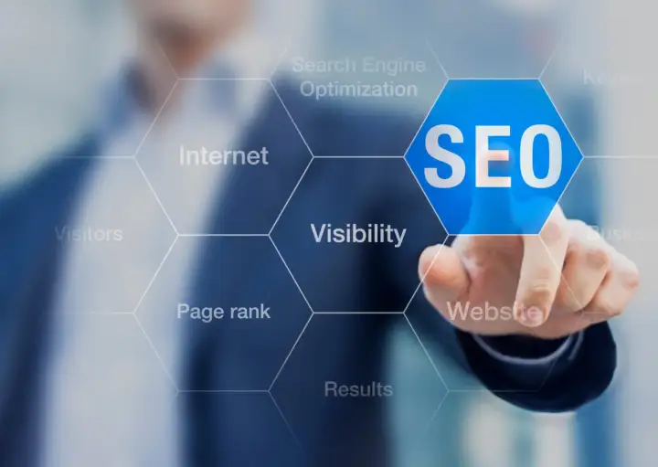 Palec wskazuje na niebieski sześciokąt z napisem SEO. Wokół widoczne są hasła: Internet, Search Engine Optimization, Keywords, Visibility, Website, Results, Page rank, Visitors. To podpowiedź, jak zbadac element.