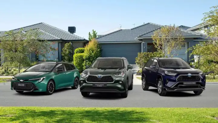 Trzy modele toyoty crossover: zielona Corolla Touring Sports, ciemnozielony Highlander Hybrid i granatowy RAV4 Plug-in Hybrid, stoją przed domami.