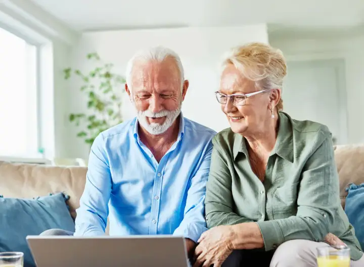 Uśmiechnięta para seniorów sprawdza na laptopie, jak sprawdzić kolejkę do sanatorium NFZ.