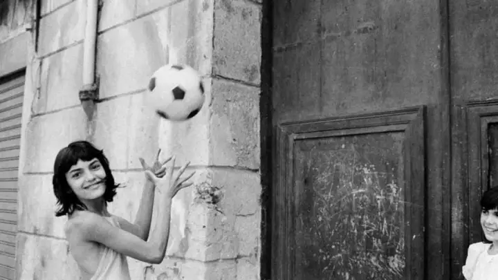 Letizia Battaglia giovane gioca con un pallone, un'immagine che cattura la spensieratezza dell'infanzia.