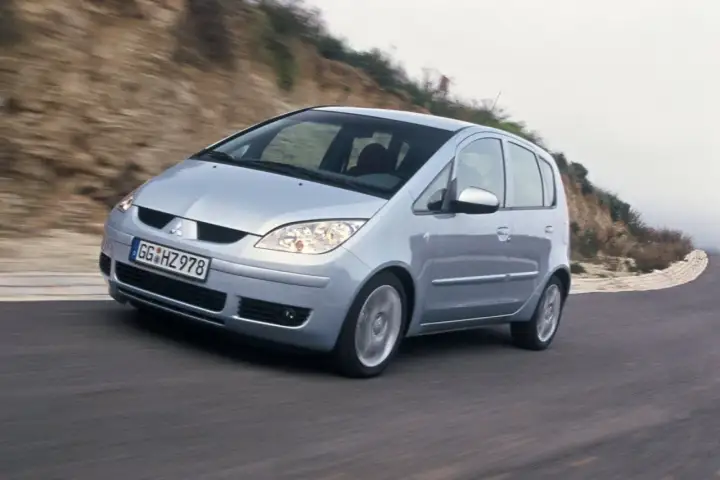 Srebrny Mitsubishi Colt VI pokonuje zakręt na krętej drodze, otoczony przez wzgórza.