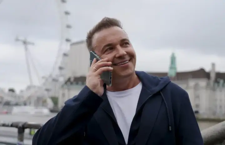 Uśmiechnięty mężczyzna rozmawia przez telefon. W tle widać London Eye. Weekend, halo, tu Londyn!