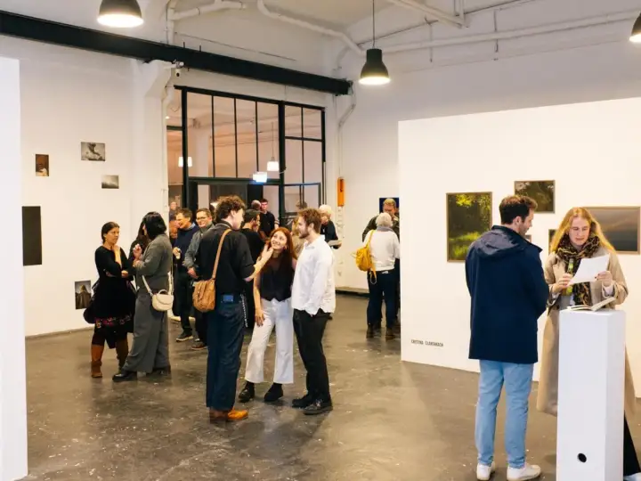 Besucher auf einer **Foto Messe Hamburg** diskutieren Kunstwerke in einer hellen Galerie.