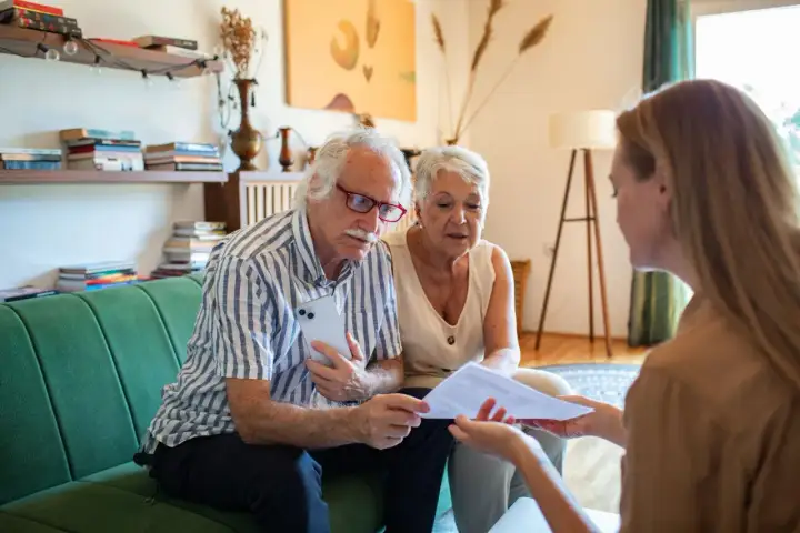 Un couple âgé discute avec une conseillère des modalités de calcul du paiement d'une maison de retraite par les descendants.