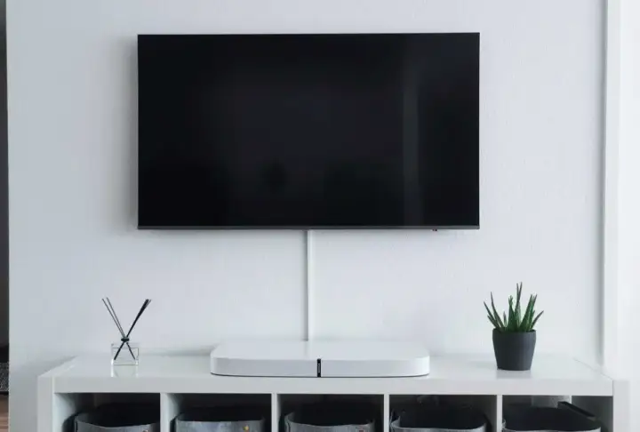 Minimalistyczny salon z telewizorem zamontowanym na ścianie. Pod nim biała szafka z ozdobami i schowkami. Idealna na jakiej wysokości telewizor.