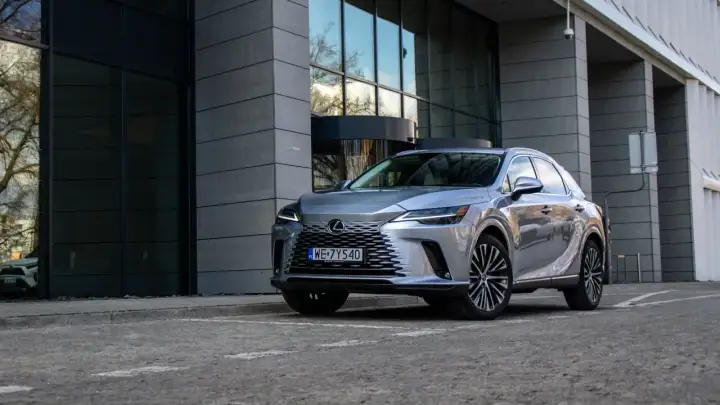 Elegancki, srebrny Lexus RX 350h zaparkowany przed nowoczesnym budynkiem z przeszkloną fasadą.