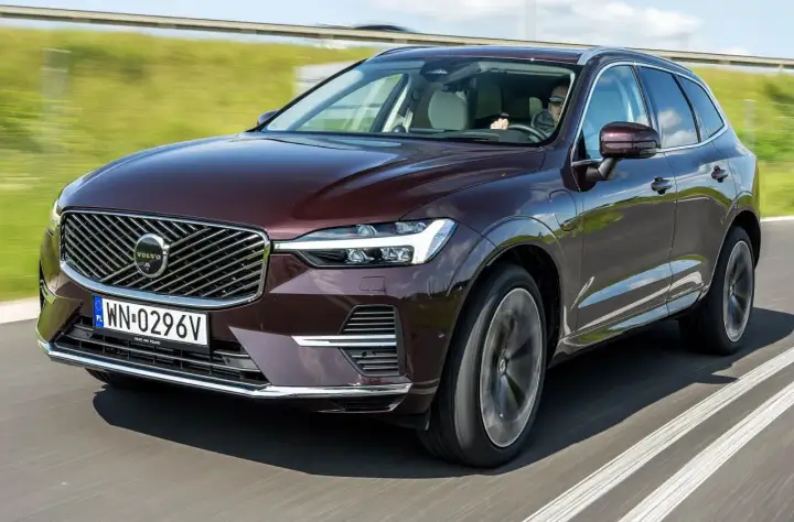 Elegancki, bordowy Volvo XC60 T5 w ruchu drogowym. Kierowca w okularach prowadzi SUV-a po asfaltowej drodze, otoczonej zielenią.