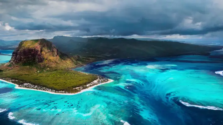 Podwodny wodospad w **Oceania** przy Le Morne Brabant, Mauritius. Turkusowa woda, góra i chmury.