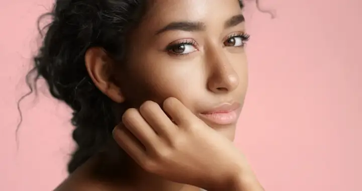 Portrait d'une jeune femme à la peau de couleur de peau olive, aux cheveux sombres et bouclés, posant sa main sur sa joue.