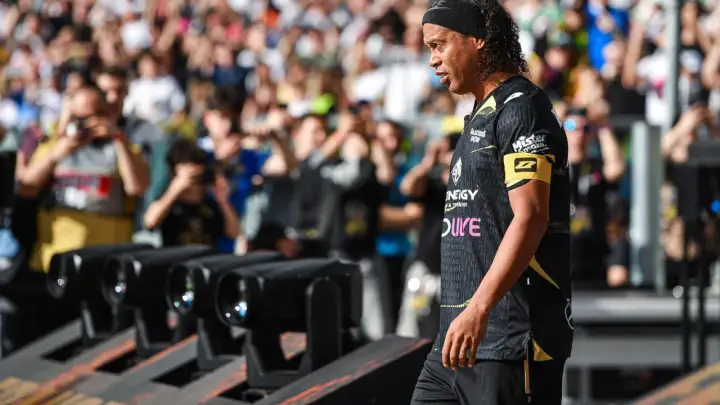 Ronaldinho w czarnej koszulce z żółtym opaską na ramieniu, z tłumem w tle.