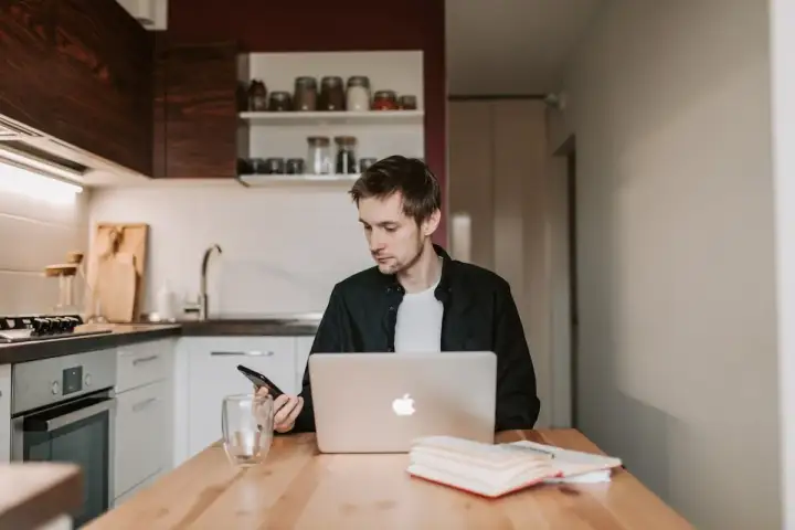 Mężczyzna w kuchni sprawdza telefon, bo Netia brak internetu uniemożliwia pracę na laptopie.