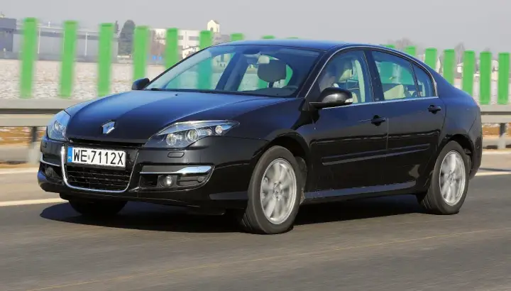 Czarny Renault Laguna 3 2.0 dCi jedzie po drodze, za zielonymi słupkami.