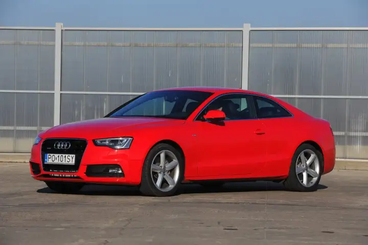 Czerwone Audi S5 z 2014 roku, sportowe coupe z elegancką linią, zaparkowane przed nowoczesnym budynkiem.