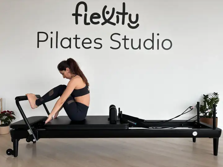 Kobieta ćwiczy na reformerze. Widoczne napisy "Flexity Pilates Studio". To dowód na pilates efekty po miesiącu.