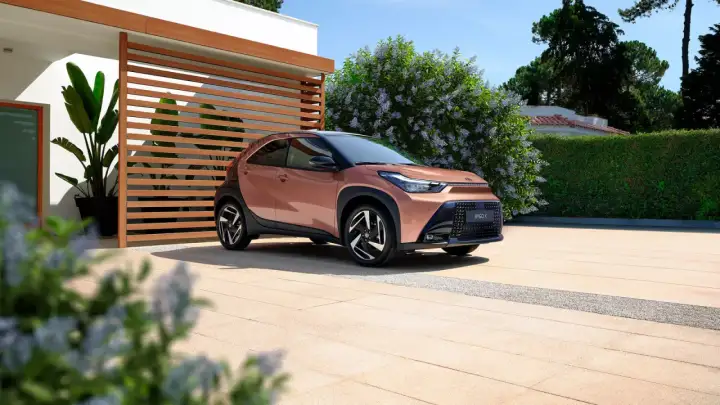 Różowy Toyota Aygo X na podjeździe przed nowoczesnym domem. Sprawdź atrakcyjną toyota aygo x cena!