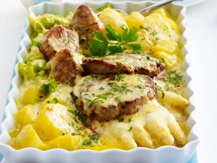 Herzhafte Spargelgerichte mit Fleisch: zarte Medaillons auf Kartoffeln und Spargel, überbacken mit Käse und garniert mit Petersilie.
