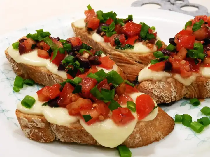 Bruschetta z pomidorami i mozzarellą: chrupiące grzanki z roztopionym serem, świeżymi pomidorami, oliwkami i szczypiorkiem. Idealny przepis na szybką przekąskę.