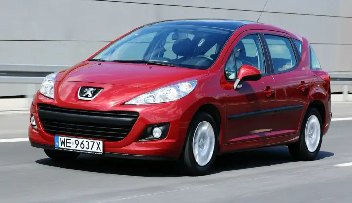 Czerwony Peugeot 207 1.6 HDi w ruchu, z widocznym logo marki i tablicą rejestracyjną.